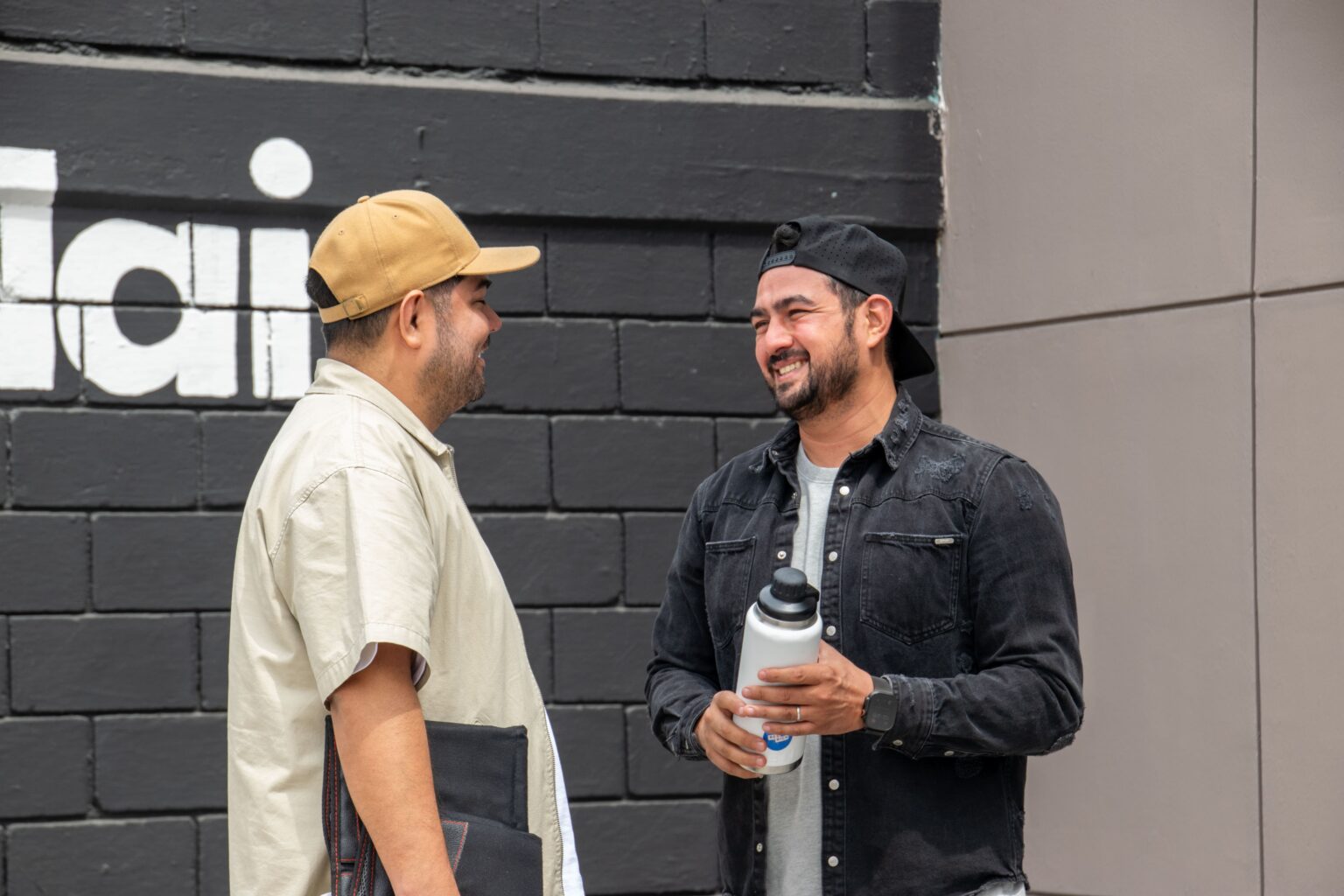 Dos hombres conversando recargados en una pared con el logo de vidain