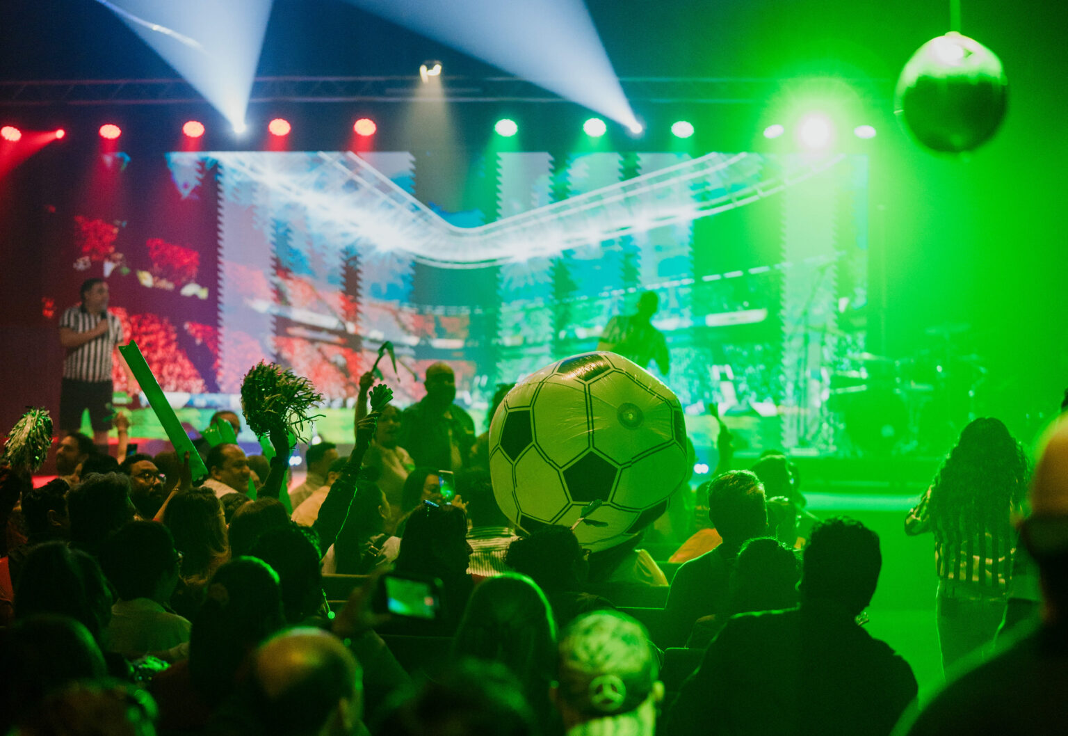Auditorio de vidain Saltillo lleno, iluminado de verde, con un balón gigante entre la gente